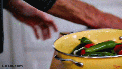 A Yellow Pot Filled With Green And Red Peppers Is Being Stirred By A Person GIF