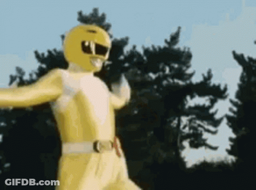A Yellow Power Ranger Is Standing In Front Of A Forest . GIF