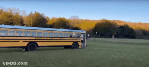 A Yellow School Bus Is Driving Through A Green Field GIF