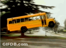A Yellow School Bus Is Hanging Upside Down On The Side Of The Road GIF