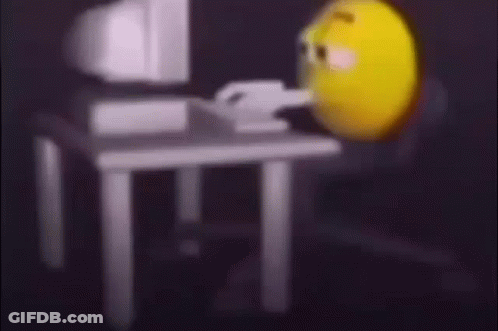 A Yellow Smiley Face Is Sitting In Front Of A Computer Monitor . GIF