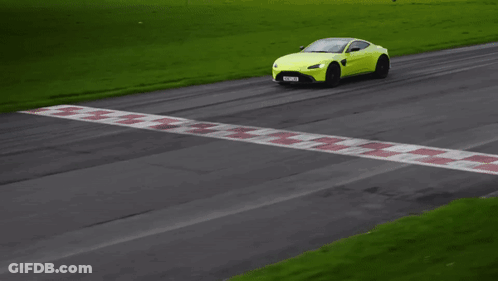 A Yellow Sports Car Is Driving Down A Road With Grass In The Background GIF