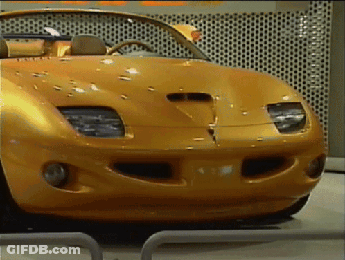 A Yellow Sports Car Is Parked In Front Of A Wall That Has Holes In It GIF