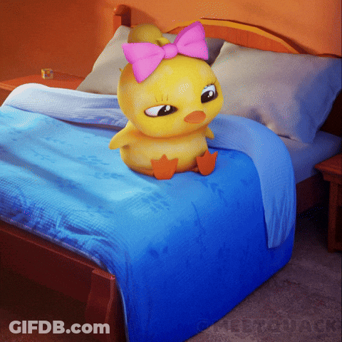 A Yellow Stuffed Duck With A Pink Bow On Its Head Sits On A Bed GIF
