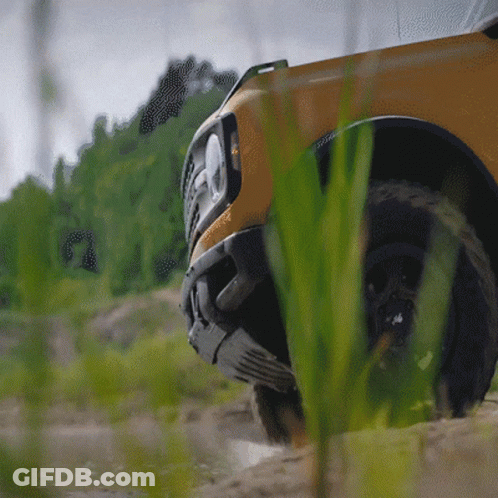 A Yellow Truck Is Driving Through A Grassy Area With Trees In The Background GIF