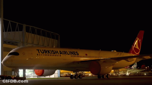 A Yellow Turkish Airlines Plane Is Parked In A Hangar At Night GIF