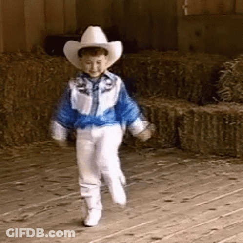 A Young Boy Dressed As A Cowboy Is Dancing In Front Of Bales Of Hay GIF