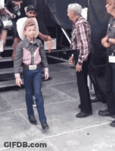 A Young Boy Dressed As A Cowboy Is Walking In Front Of A Group Of People . GIF