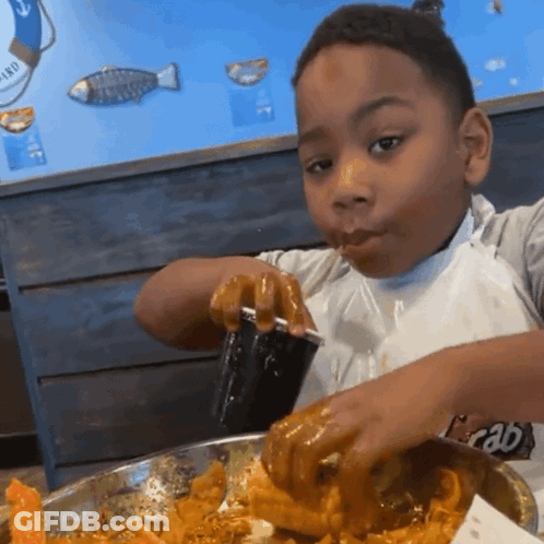 A Young Boy Eating Food With A Cup That Says Crab On The Front GIF