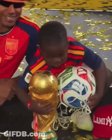 A Young Boy Holds A Soccer Ball In Front Of A Trophy That Says Lamin GIF