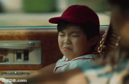 A Young Boy In A Baseball Cap Is Sitting In The Back Seat Of A Car Making A Funny Face . GIF