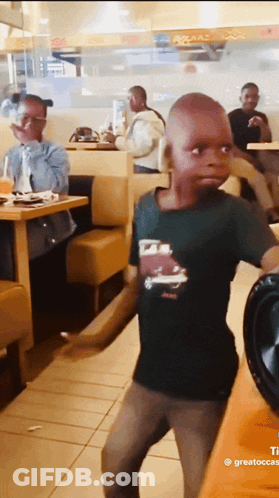 A Young Boy In A Black Shirt With A Car On It Is Dancing In A Restaurant GIF