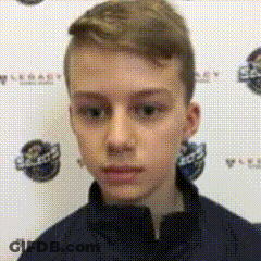 A Young Boy In A Blue Jacket Is Standing In Front Of A Wall With A Logo On It . GIF