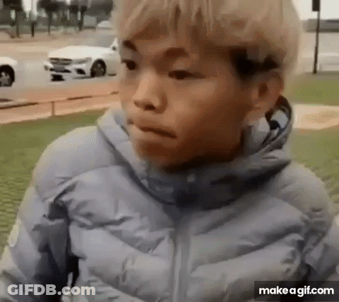 A Young Boy In A Blue Jacket Is Standing In Front Of A White Car And Making A Funny Face . GIF