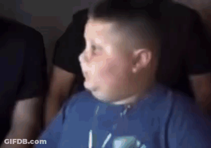 A Young Boy In A Blue Shirt Is Making A Funny Face While Sitting In A Dark Room . GIF