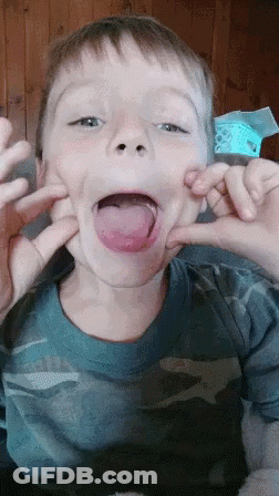 A Young Boy In A Blue Shirt Is Making A Funny Face With His Tongue Out GIF