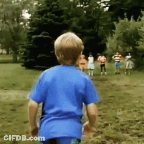 A Young Boy In A Blue Shirt Is Running Towards A Group Of Children In A Park . GIF