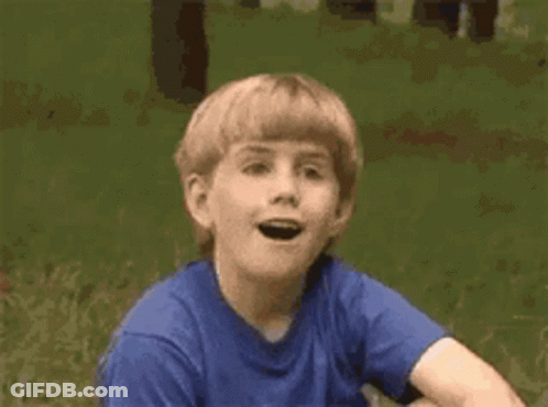 A Young Boy In A Blue Shirt Is Sitting In The Grass . GIF