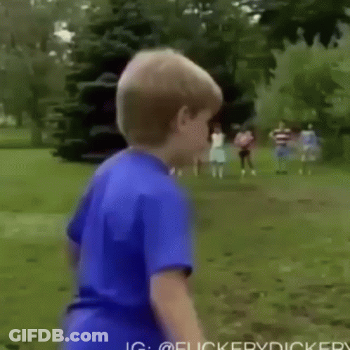A Young Boy In A Blue Shirt Is Standing In A Field With Trees In The Background . GIF