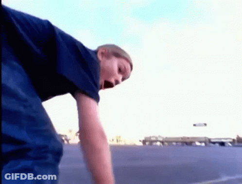 A Young Boy In A Blue Shirt Is Standing In A Parking Lot GIF
