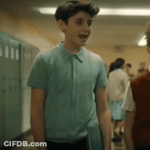 A Young Boy In A Blue Shirt Is Walking Down A Hallway With Other Children . GIF