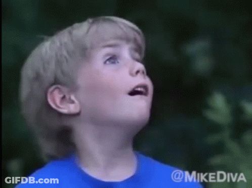 A Young Boy In A Blue Shirt Looks Up At The Sky GIF