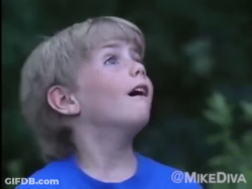 A Young Boy In A Blue Shirt Looks Up At The Sky GIF