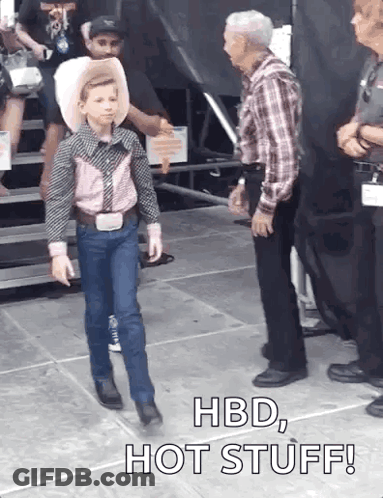 A Young Boy In A Cowboy Outfit Is Walking In Front Of A Man With The Words Hbd Hot Stuff Written On The Ground GIF