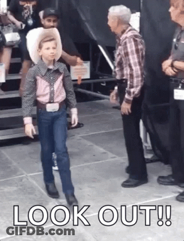 A Young Boy In A Cowboy Outfit Is Walking On A Stage While Talking To A Man . GIF