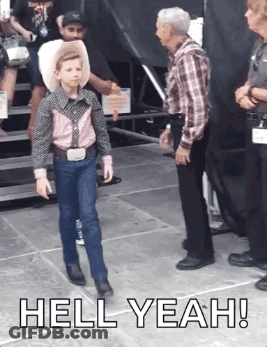 A Young Boy In A Cowboy Outfit Is Walking On A Stage With The Words Hell Yeah Written Below Him GIF