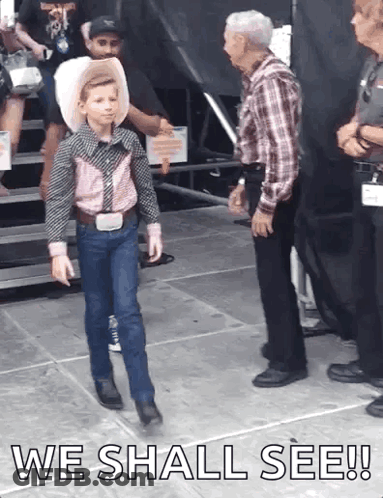 A Young Boy In A Cowboy Outfit Is Walking On A Stage With The Words " We Shall See " Above Him GIF