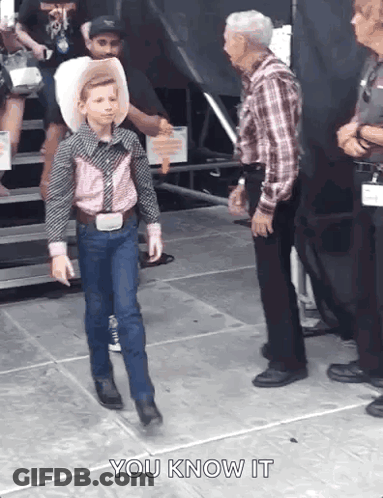 A Young Boy In A Cowboy Outfit Is Walking Towards A Man In A Plaid Shirt . GIF