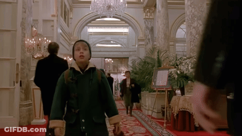 A Young Boy In A Green Coat Is Walking Through A Hallway GIF