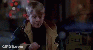 A Young Boy In A Jacket Is Standing In Front Of A Christmas Tree And A Car . GIF