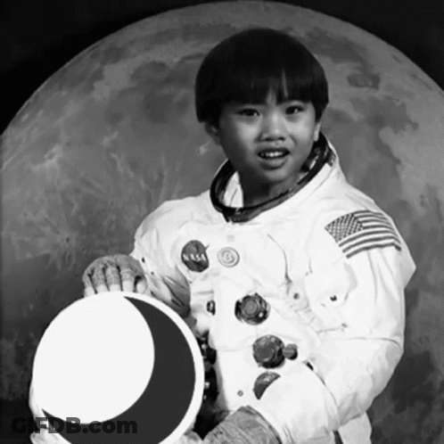 A Young Boy In A Nasa Space Suit Is Holding A Crescent Moon GIF