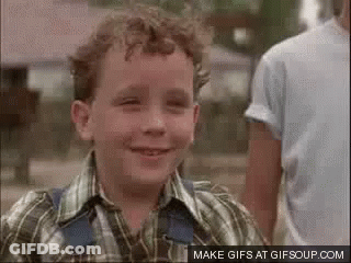 A Young Boy In A Plaid Shirt And Overalls Is Smiling . GIF