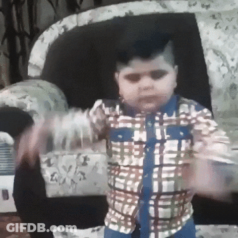 A Young Boy In A Plaid Shirt Is Standing In Front Of A Couch . GIF