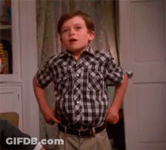 A Young Boy In A Plaid Shirt Is Standing In Front Of A Door Holding A Spoon And Saying `` Fashion '' . GIF