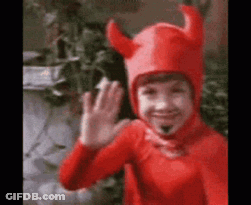 A Young Boy In A Red Devil Costume Is Waving . GIF