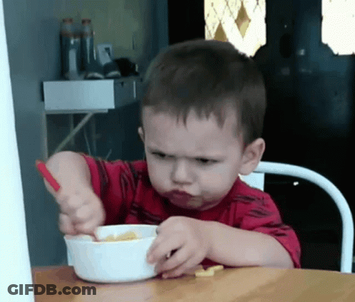 A Young Boy In A Red Shirt Is Eating Cereal With A Spoon GIF
