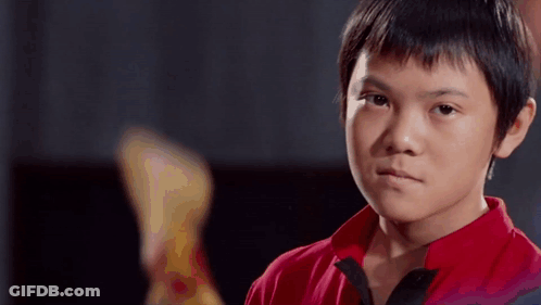 A Young Boy In A Red Shirt Is Looking At The Camera With A Serious Expression On His Face . GIF
