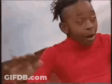 A Young Boy In A Red Shirt Is Making A Funny Face While Looking At The Camera . GIF