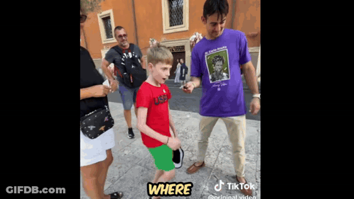 A Young Boy In A Red Shirt Is Standing Next To A Man In A Purple Shirt . GIF