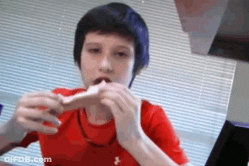 A Young Boy In A Red Under Armour Shirt Is Eating A Sandwich GIF