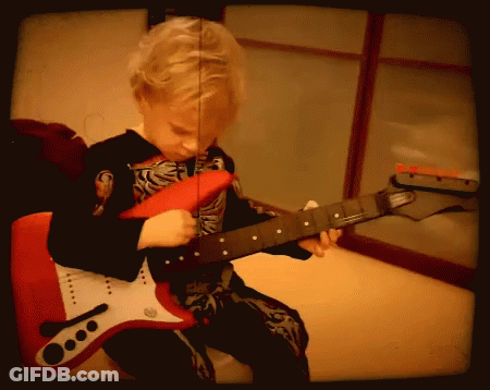 A Young Boy In A Skeleton Costume Is Playing A Red Electric Guitar GIF
