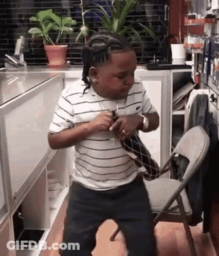 A Young Boy In A Striped Shirt Is Dancing In A Kitchen Next To A Chair . GIF