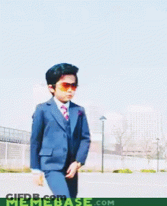 A Young Boy In A Suit And Tie Holds A Pair Of Glasses In Front Of A Memebase.com Logo GIF