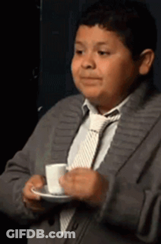 A Young Boy In A Suit And Tie Is Holding A Cup Of Coffee On A Saucer . GIF