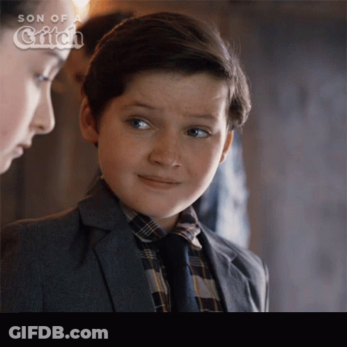 A Young Boy In A Suit And Tie Stands Next To A Woman In A Son Of A Witch Ad GIF