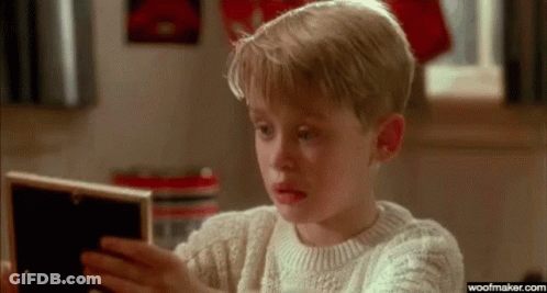 A Young Boy In A Sweater Is Looking At A Picture In A Frame . GIF